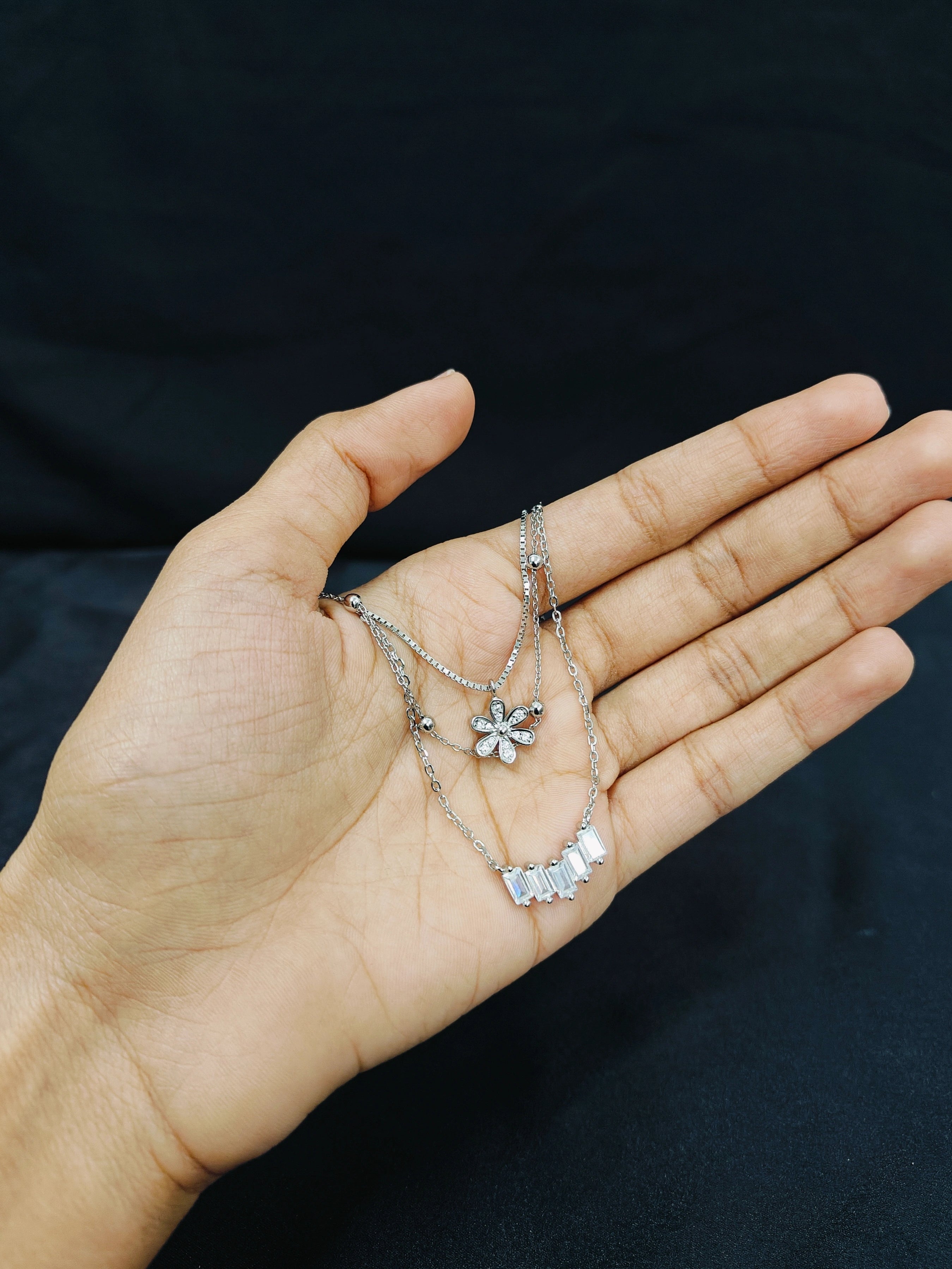 Hand holding a silver necklace with floral pendants against a dark background